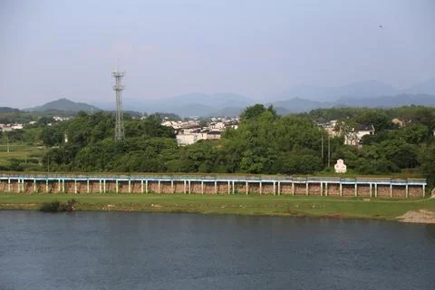 Riverfront landscape with a long elevated walkway, communication tower, vil.. Stock Photos