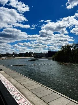 Riverfront promenade under dramatic blue sky and fluffy clouds with urban s.. 写真素材