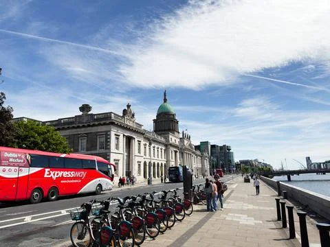 Riverfront street scene with rental bikes, red Expressway coach and the Cus.. Stock Photos