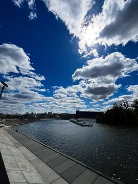 Riverfront under dramatic blue sky with fluffy clouds and sunlit water in a.. 写真素材