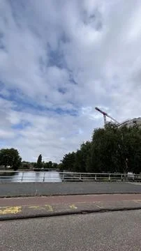 Riverside bridge beside red construction crane, urban road, trees, and distant Stock Photos