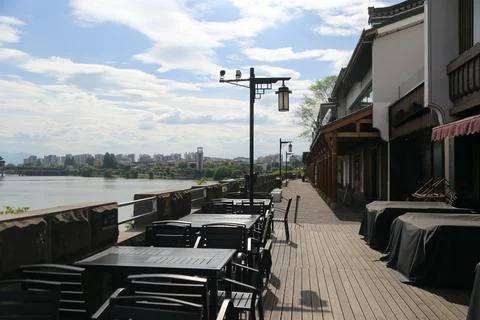 Riverside outdoor dining terrace with empty tables beside calm water and di.. Stock Photos