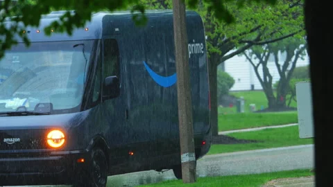 Rivian electric delivery Amazon van driving through heavy rain in suburban Stock Footage 335968753