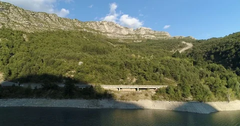 Road alongside artificial lake at the bottom of rocky mountain  drone aerial 4k Stock Footage 125755299