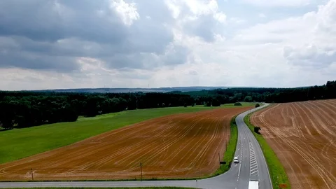 A road among red empty fields, green meadows an forests. Stock Footage 114982721