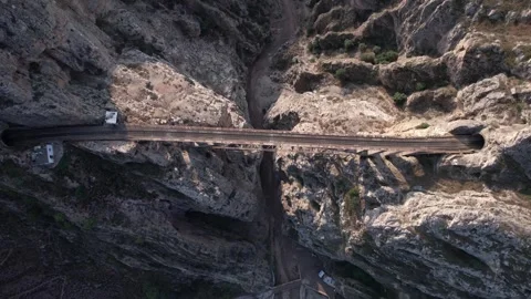 Road and tunnel cut through rocky canyon walls with vehicles under cloudy sky Stock Footage 342705568