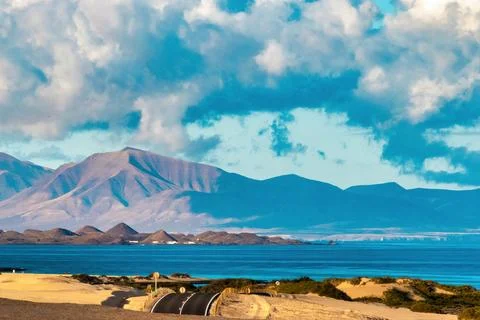 Road by the beach with mountains and clouds in the background during daytime Stock Photos