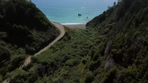 Road bends through mountains towards a terquoise ocean Stock Footage 152766987