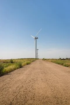 Road between green fields and wind turbines on blue sky background Stock Photos