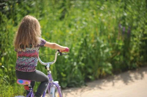 The road to childhood - a girl rides a bike on a rural road Stock Photos