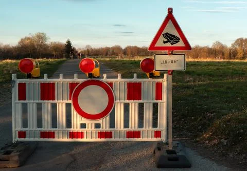 Road closure sign blocking access with warning of frogs in the evening. Stock Photos