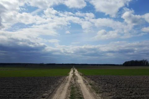 Road to the clouds, passes through a plowed field Stock Photos