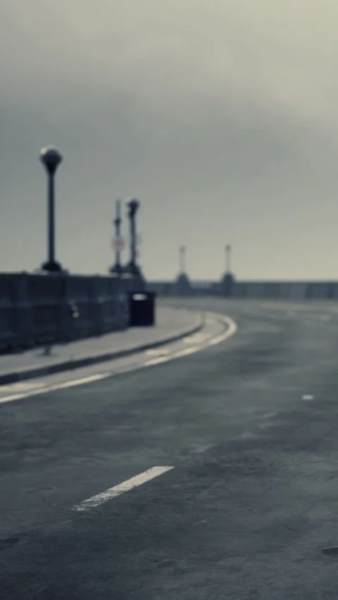 Road on a cloudy day with no vehicles and a lone lighthouse in the distance Stock Footage 346758884