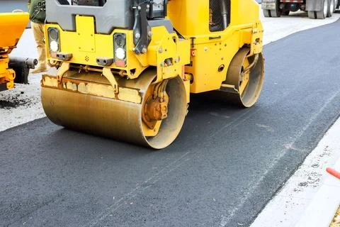 Road construction crew uses heavy roller to compact asphalt on new road surface Stock Photos