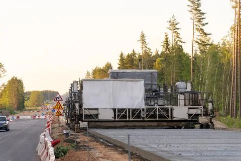 Road construction machine paving a highway section beside forest Stock Photos