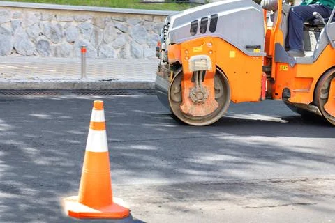 Road construction roller in motion rams fresh asphalt on the roadway. Stock Photos
