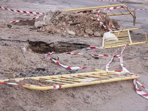 Road construction site with broken asphalt, safety barriers, and warning ta.. Stock Photos
