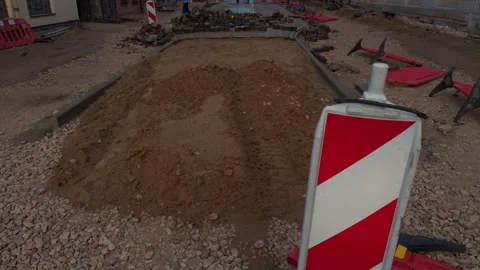 Road construction site with excavated soil mound, paving blocks, red warning Stock Footage 345128236