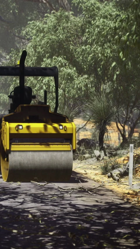 Road construction uses a yellow steamroller on a dirt path surrounded by trees Stock Footage 334883490
