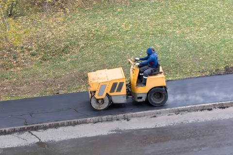 Road construction worker compactes fresh steaming asphalt Stock Photos