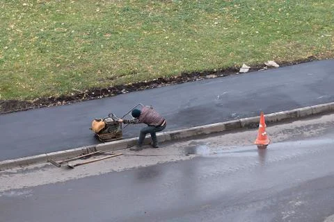 Road construction worker compactes fresh asphalt with handheld mini roller Stock Photos