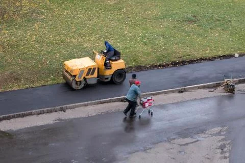 Road construction worker compactes fresh asphalt with roller compactor Stock Photos