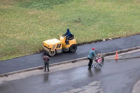 Road construction worker compactes fresh asphalt with roller compactor Stock Photos