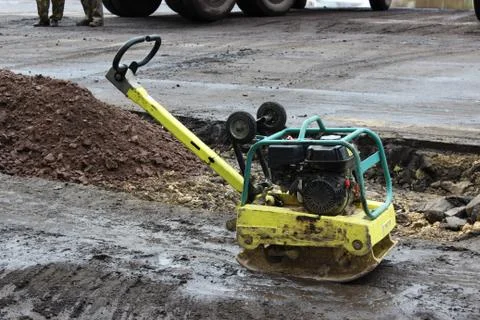 A road construction worker compacts the soil with a compact vibroplate before Stock Photos