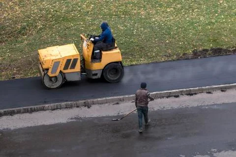 Road construction worker drives roller compactor machine Stock Photos