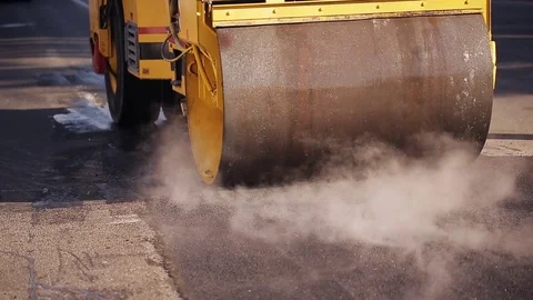 Road construction worker leveling asphalt using rake while in the back road Stock Footage