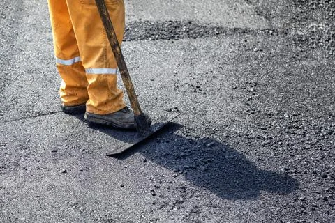 Road construction worker leveling fresh asphalt pavement Stock Photos