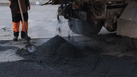 Road construction worker shoveling a pile of fresh hot asphalt from dump truc Stock Footage 339801852