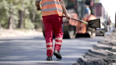 Road Construction Worker Is Walking With A Shovel On A Tarmac Road Stock-Footage 142349250