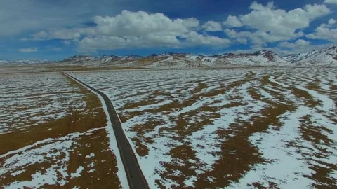 Road cuts through a snow covered field under a cloudy sky Stock Footage 311820324