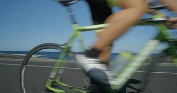 A road cyclist powers past the camera in slow motion with whip pan. Vídeo Stock 86129875