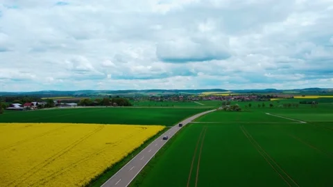 Road into the distance through a rapeseed field with clouds 動画素材 154373992
