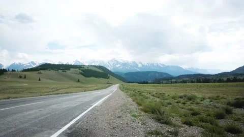 Road in the field on the background of snow-capped mountain peaks. Scene. Alps Stock Footage 137337654