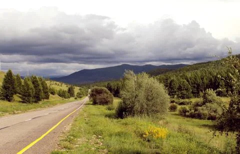 Road in forest under a blue sky with white clouds Sayan mountains Siberia Rus Stock Photos