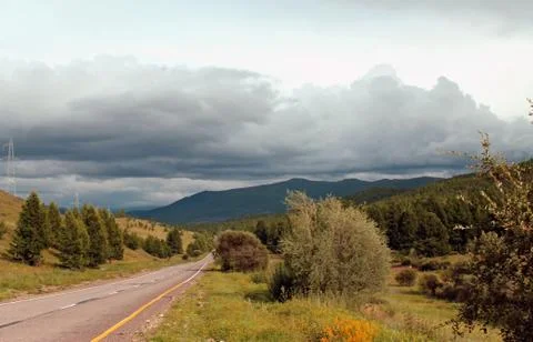 Road in forest under a blue sky with white clouds Sayan mountains Siberia Rus Stock Photos