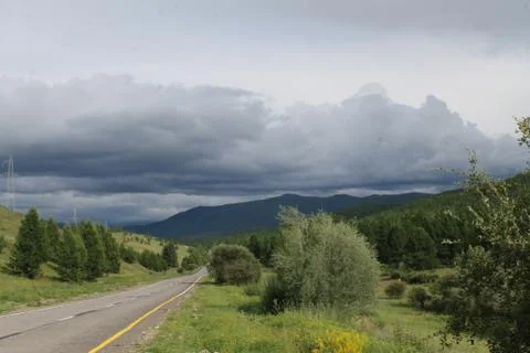 Road in forest under a blue sky with white clouds Sayan mountains Siberia Rus Stock Photos
