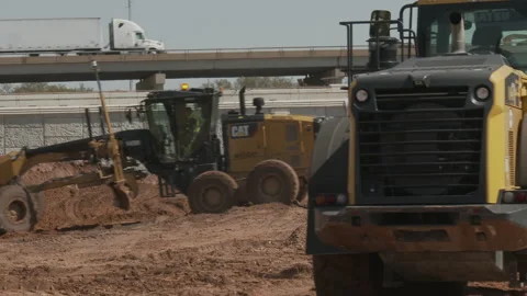 Road grader and frontend load move dirt beneath busy highway, 4K. Stock Footage 151601680