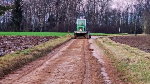 Road grading tractor leveling muddy rural dirt road during maintenance work in Видео 325833379