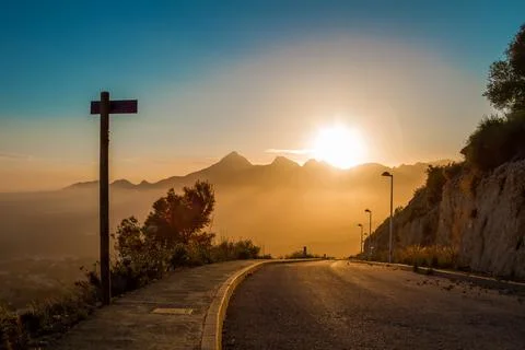 Road with an index post sign down on the horizon with the setting sun. Stock Photos