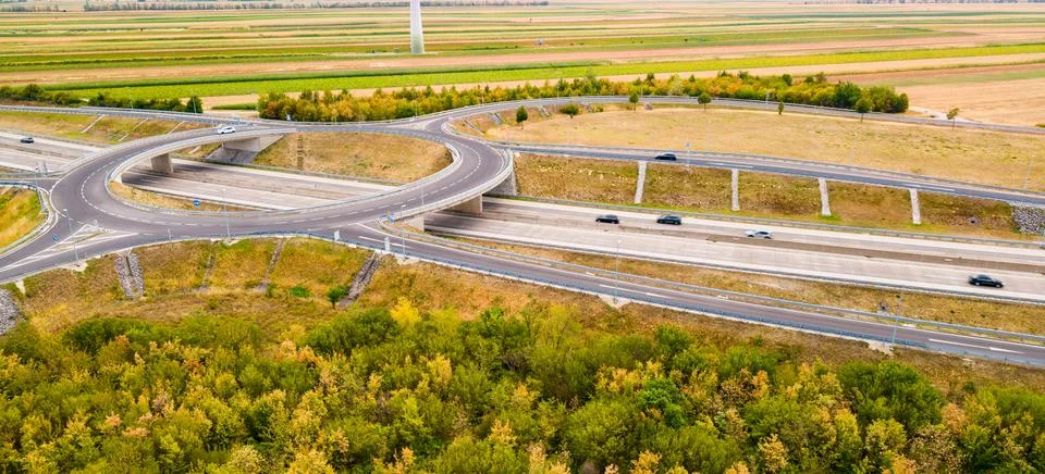 Road intersection near fields with trees and cars in view during daytime. C.. Stock Photos