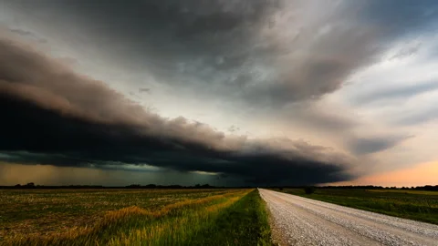 Road leading across fields as a powerful storm clouds full of color moves ov Stock Footage 285935382