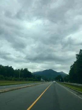 Road Leading to Dark Clouds Over Mountains Stock Photos