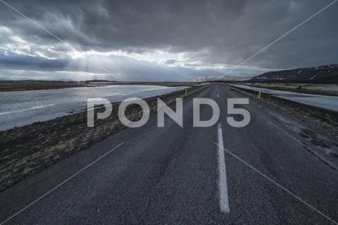Road leading into the dramatic landscape of Iceland while the sun shines through Stock Photos