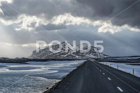 Road leading into the dramatic landscape of Iceland while the sun shines through Stock Photos