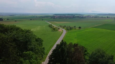 Road leading through the forest and fields to a small village on the plain 動画素材 155596173