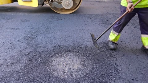 Road maintenance worker sweeping fresh warm mix asphalt with a road roller Stock Footage 253230879